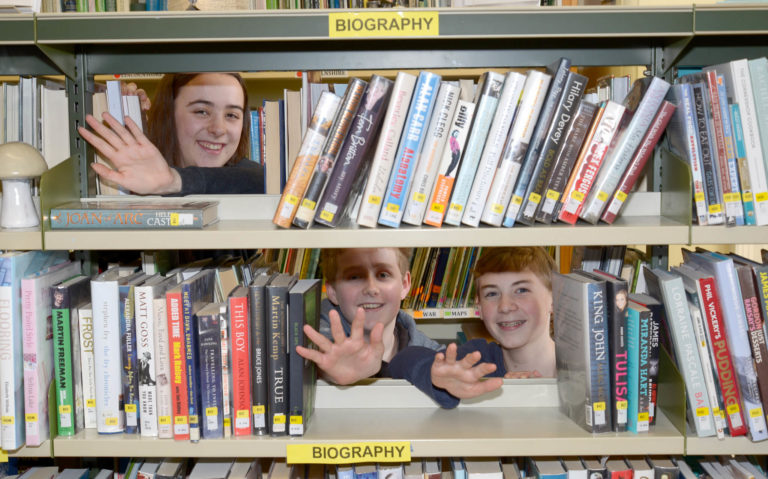 teens waving through bookshelf